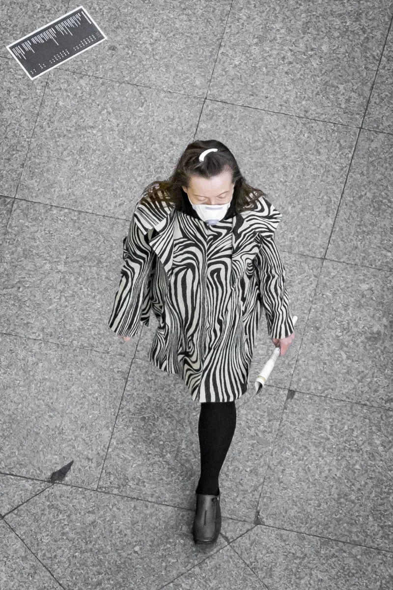 Overhead view of a masked woman in a zebra-striped coat walking across stone pavement